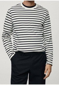 Camicetta bianca a maniche lunghe con righe orizzontali blu navy, scollatura rotonda, vestibilità slim, abbinata a pantaloni neri, texture del tessuto liscia.