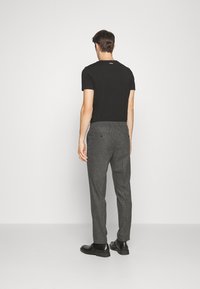 Černé přiléhavé tričko a šedé kalhoty s tapered střih s texturovaným povrchem. Černé boty doplňují outfit. Minimalistický design, bez viditelných log.