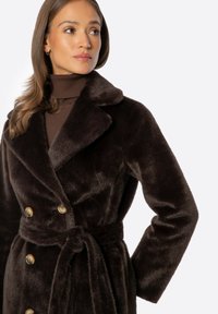 Abrigo de piel sintética marrón de doble botonadura con un gran cuello, dos botones y un cinturón a juego, que presenta una textura suave y aterciopelada.