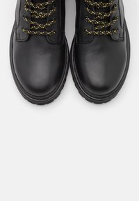 Botas de ankle de cuero negro con puntera redondeada, superficie texturizada y cordones moteados de amarillo a través de ojales metálicos.