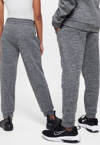 Twee mensen in grijze sweats en zwarte Nike sneakers, vanaf de taille naar beneden gefotografeerd tegen een effen achtergrond.