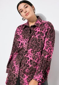Rosa Leopardenmusterhemd mit langen Ärmeln, Knopfverschluss und Brusttasche. Aus weichem Stoff gefertigt, mit einem schwarzen Leopardenmuster auf rosa Hintergrund.