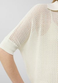 Sweter dzianinowy, w oversize'owym kroju w kolorze ecru, o luźnym, otwartym splotem i ribbowanych mankietach. Posiada kołnierz i luźny krój.