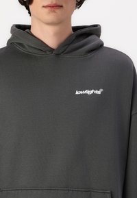 Dark gray hoodie with a soft texture, featuring a front pocket and a small white branded logo on the left chest area.