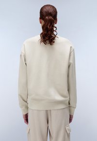 Beige sweater met een ronde hals en geribbelde zoom. Zachte textuur, nauwsluitende mouwen en een minimalistisch merkdetail op de linkerschouder.