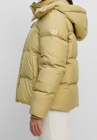 Jasnożółta kurtka puchowa z kapturem, pikowany design i kwadratowa naszywka z logo na rękawie. Teksturowany materiał z prążkowanymi mankietami.