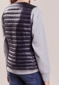 Padded jacket with a gray sweatshirt front and a black, quilted, shiny back. Features ribbed cuffs and a round neckline.