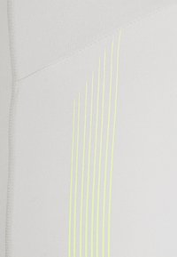 Zbliżenie białej tkaniny z ukośnym przeszyciem i ośmioma pionowymi, równolegle biegnącymi neonowymi żółtymi liniami jako detal wzoru.