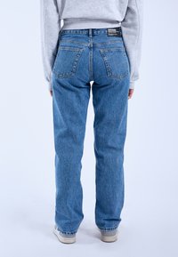 Blue denim jeans with a relaxed fit, high waist, and two back pockets. Features a subtle faded texture and contrasting stitching.