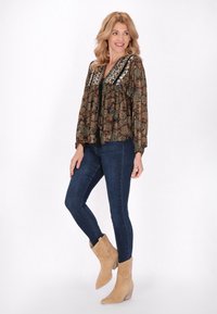 Bluză cu mâneci lungi, neagră și maro cu model, cu decolteu în V și guler împodobit, asociată cu blugi skinny închisi la culoare și bocanci bej până la gleznă.