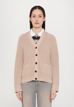 Beige knitted cardigan with a V-neck, black buttons, and two front pockets. Worn over a collared checkered shirt. Smooth texture.