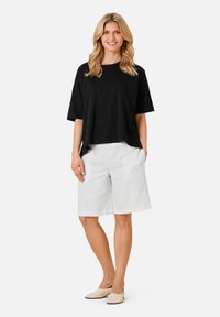 Zwarte korte mouwen top met een relaxte pasvorm, gecombineerd met witte knielange shorts. De shorts hebben een gladde textuur en zijzakken.