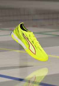 Hellgelber Sportschuh mit strukturiertem Obermaterial, schlankem Design, weißer Außensohle und roten Akzenten an der Seite.