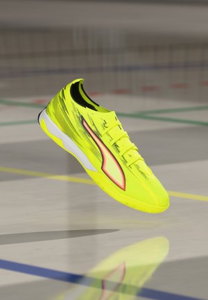 Hellgelber Sportschuh mit strukturiertem Obermaterial, schlankem Design, weißer Außensohle und roten Akzenten an der Seite.