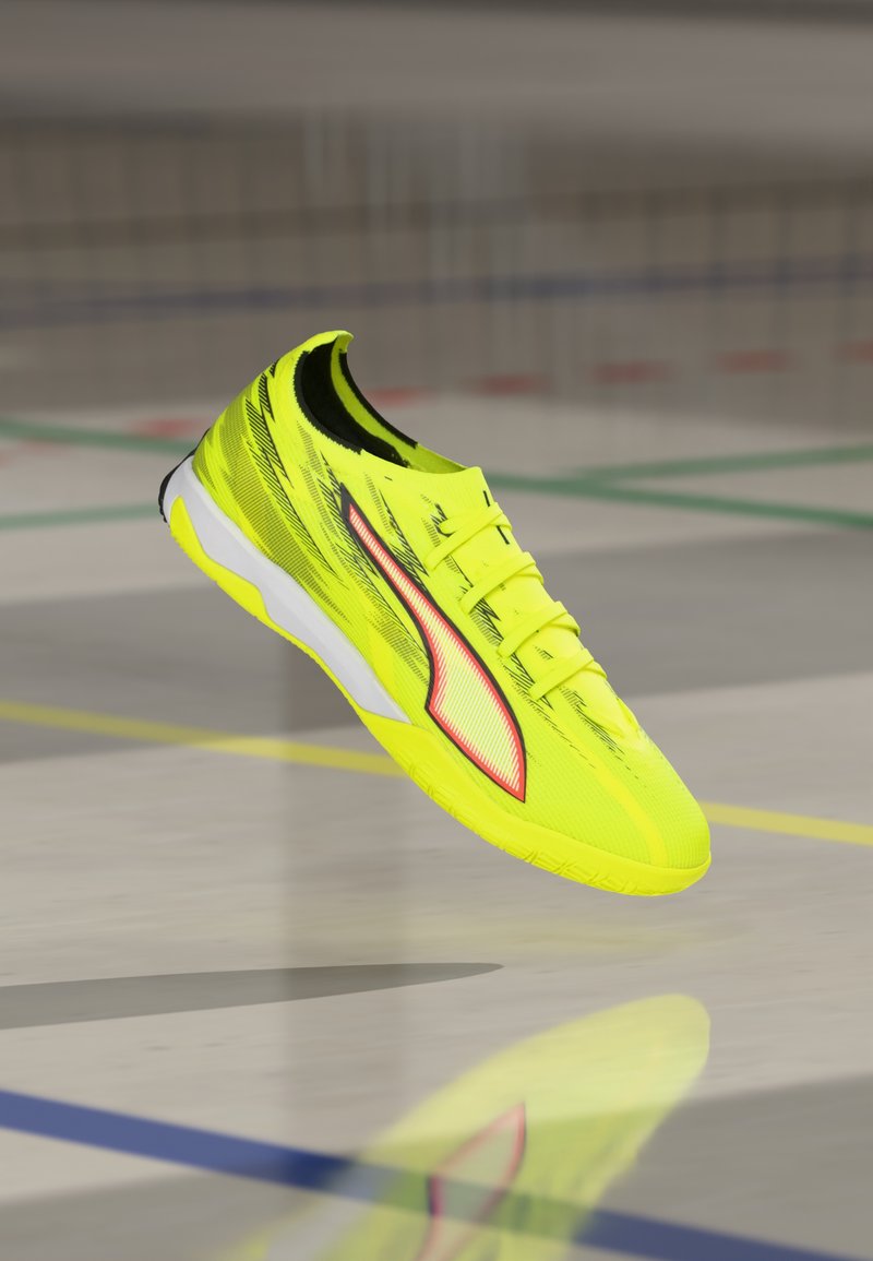 Hellgelber Sportschuh mit strukturiertem Obermaterial, schlankem Design, weißer Außensohle und roten Akzenten an der Seite.