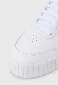Tenis alb din piele, cu o suprafață texturată, vârf rotunjit, detalii perforate și o talpă groasă din cauciuc alb, cu striții orizontale.