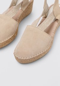 Zapatos de cuña de ante beige con punta redonda, correas elásticas y suelas envueltas en yute. Textura suave y detalle de costura sutil.