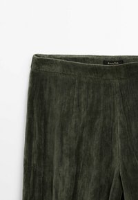 Pantalon vert foncé à texture veloutée avec une taille haute et des coutures verticales subtiles présenté sur un fond blanc.