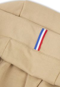 Tela beige con una textura suave, que presenta una cinturilla doblada con un acento de rayas verticales en rojo, blanco y azul.