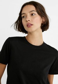 T-shirt en coton noir avec un col rond et des manches courtes. Texture lisse, design simple sans motifs ni embellissements.
