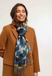 Écharpe multicolore aux teintes bleues, brunes et orange avec une finition texturée. Présente des bords frangés et une étiquette de marque en bas.