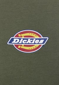 Olive green T-shirt featuring a circular logo with a red background, yellow accents, and the word "Dickies" in bold blue letters.