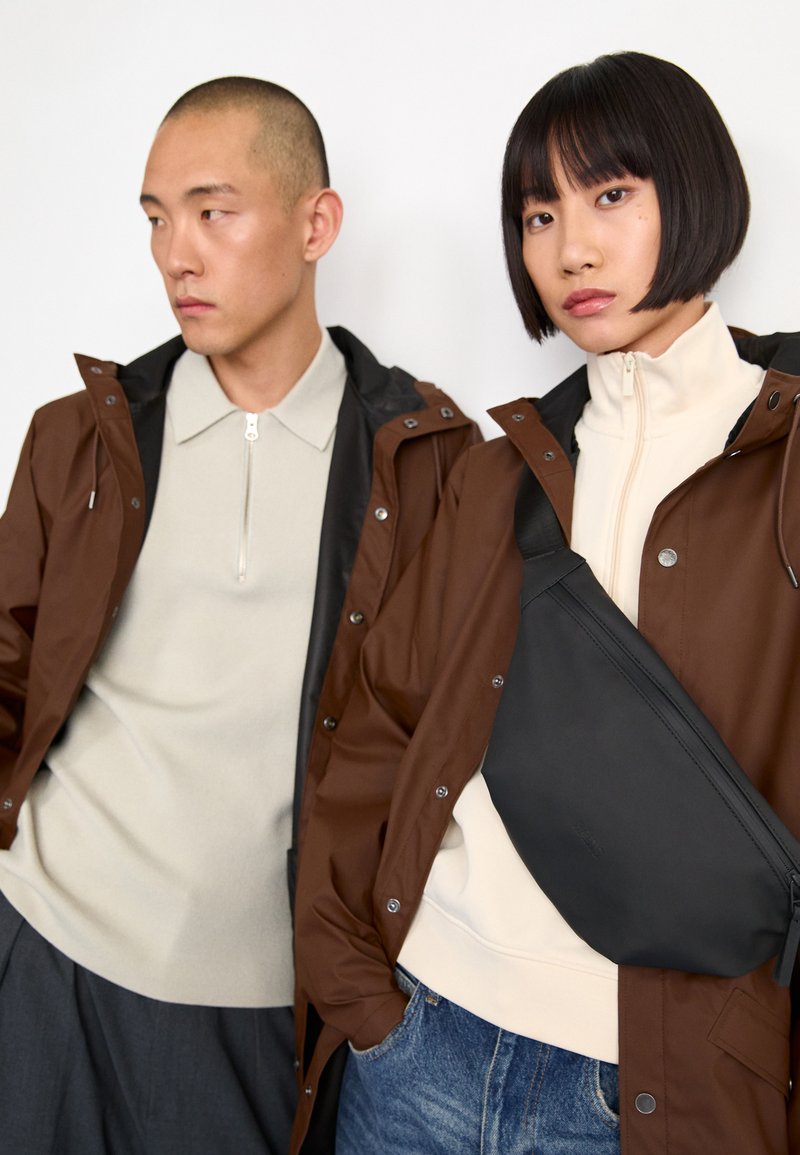 Two models wear outerwear: a brown waterproof jacket and a cream zip-up fleece, paired with a black crossbody bag and denim.