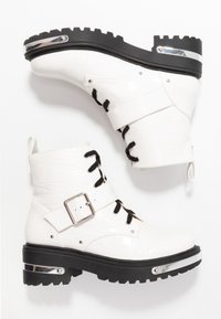 Bottes blanches à la cheville avec une texture crocodile, lacets noirs, boucle latérale, semelle noire épaisse et accents argentés.