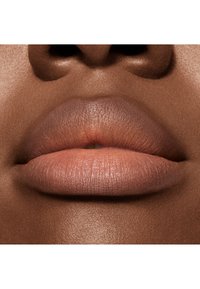 Gros plan sur des lèvres pulpeuses au fini mat dans un ton nude, sur une peau brune lisse, mettant en valeur la texture et la forme naturelles.