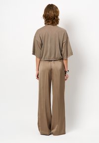 Bronzen cropped top met brede mouwen, gecombineerd met hooggetailleerde, vloeiende beige broek. Glad, lichtgewicht stof met een relaxte pasvorm.