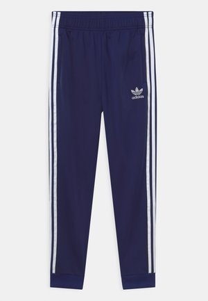 Granatowe spodnie dresowe Adidas z białymi potrójnymi paskami po bokach, elastycznym pasem, kieszeniami bocznymi i logo Adidas trefoil na lewej udzie.