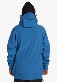 Veste imperméable bleue avec capuche, dotée d'une texture lisse, de poignets élastiques et d'une coupe décontractée, conçue pour les activités de plein air.