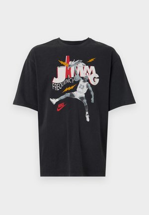 Camiseta negra de manga corta con un gráfico de un jugador de baloncesto, "JAMMING", y detalles en relámpago en rojo y amarillo. Logo de Nike presente.
