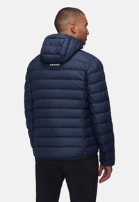 Chaqueta acolchada de color azul marino con capucha, que presenta paneles acolchados, una textura suave, puños elásticos y un detalle de logo en la parte posterior.