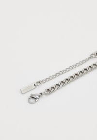 Zilveren ketting met dikke schakken en een bevestigd kreeftsluitinkje op een lichte achtergrond.
