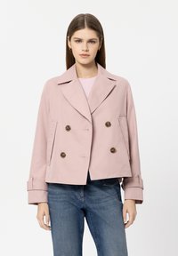Light pink double-breasted jacket with large brown buttons, wide lapels, and cuffed sleeves, paired with blue denim jeans.