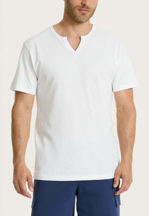 Uomo che indossa una t-shirt bianca semplice a maniche corte con scollo a V e pantaloncini blu navy, in piedi contro uno sfondo neutro.