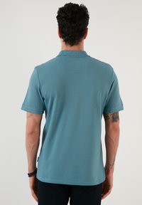 Polo cu mânecă scurtă, de culoare teal, fabricat dintr-un material texturat. Guler clasic și fără branding vizibil. Design simplu și curat.