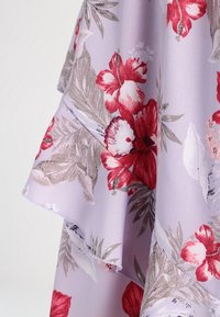 Kukkakangas lilakalla pohjalla, jossa on suuria punaisia ja valkoisia kukkia sekä vihreitä lehtiä, sileä pinta ja röyhelöreunat.