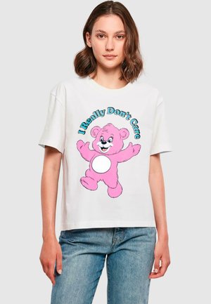 T-shirt en coton blanc avec un grand ours en cartoon rose et le texte "Je m'en fiche vraiment" en bleu au-dessus et en dessous de l'ours.