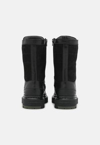 Botas negras que presentan una mezcla de materiales lisos y texturizados, una suela de goma robusta, cierre de cremallera y soporte en el tobillo reforzado.