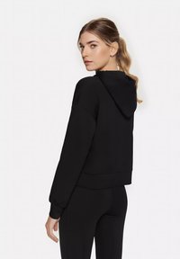 Black cropped hoodie with a drawstring hood, ribbed cuffs, and hem. Soft fabric with a smooth texture, designed for comfort and mobility.