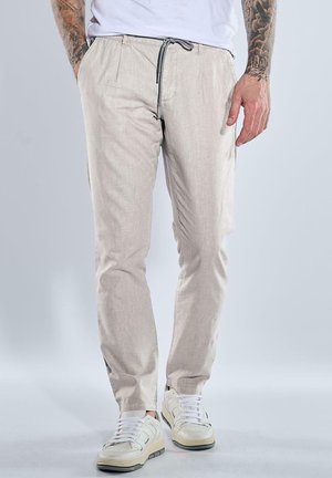 Hellbeige Baumwollmischungshose mit einem Kordelzugbund, Seitentaschen und schmalem Schnitt; getragen mit weißen Sneakers und einem einfachen weißen T-Shirt.