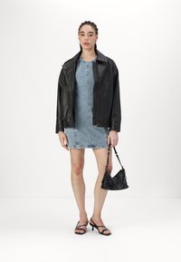 Jaqueta de couro preta sobre um vestido de ganga, acompanhada por uma pequena mala preta. O conjunto inclui saltos altos pretos com tiras e exibe uma silhueta elegante.