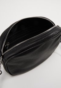 Borsa in pelle nera con finitura testurizzata, chiusura a zip e scomparti interni. Presenta accessori in argento e una forma arrotondata.