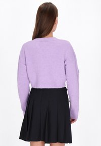 Fioletowy sweter z dzianiny o prążkowanej fakturze, z długimi rękawami i okrągłym dekoltem, zestawiony z czarną spódnicą plisowaną.