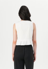 Hvid ærmeløs top med lodrette striber, der har en peplumkant. Kombineret med sorte, løstsiddende bukser for et komplet look.