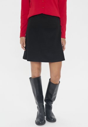 Jupe noire évasée avec une texture lisse, associée à des bottes en cuir noir montant jusqu'au genou. Le haut est une chemise ajustée à manches longues rouge.