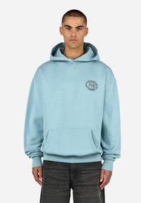 Απαλή μπλε κουκούλα, κατασκευασμένη από μαλακό ύφασμα, με μπροστινή τσέπη και κυκλικό λογότυπο στο αριστερό στήθος. Μακριά μανίκια με ριμπ τελείωμα.