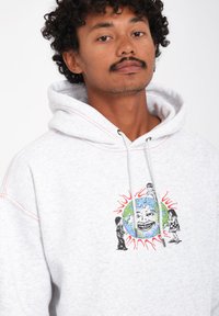 Lichtgrijze hoodie met een vooropdruk van een lachende aarde omringd door cartoonfiguren. Heeft een capuchon met trekkoord en gestikte accenten.